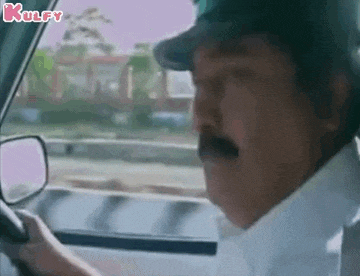 a man with a mustache is driving a car while wearing a hat .