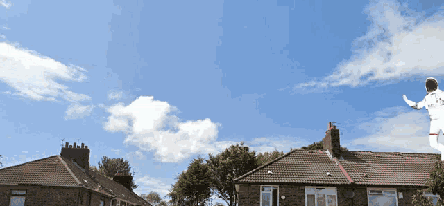 a silhouette of a person flying over a row of houses with a blue sky in the background