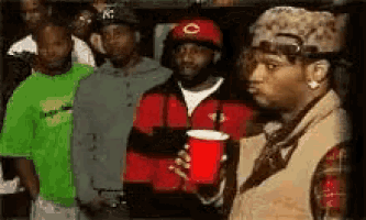 a group of men are standing next to each other in a room . one of the men is holding a red cup .