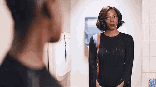 a woman in a black bodysuit is standing in front of a mirror in a bathroom .