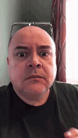a bald man wearing glasses and a black shirt is making a surprised face