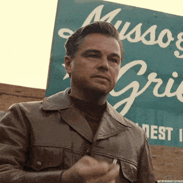 a man in a brown leather jacket is standing in front of a sign that says mussoes grill