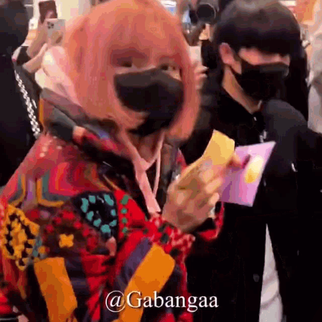 a woman with pink hair is wearing a mask and holding a card .