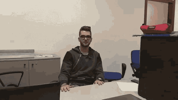a man wearing glasses sits at a desk with a laptop