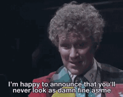 a man with curly hair is wearing a red jacket and tie and talking into a microphone in a dark room .