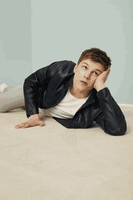 a young man in a leather jacket is laying on the floor with his hand on his face