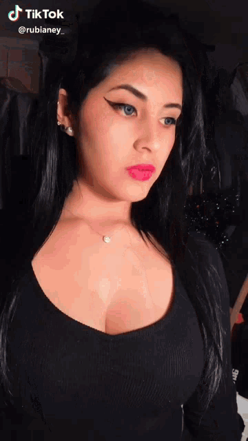 a woman wearing a black top and a necklace has a tiktok sticker on her face