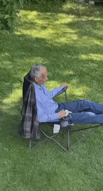 an elderly man is sitting in a folding chair on the grass .