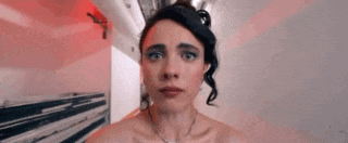 a woman is making a funny face while standing in front of a refrigerator .
