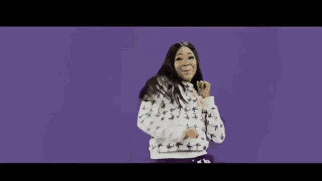 a woman in a white hoodie and purple sweatpants is dancing on a purple background .
