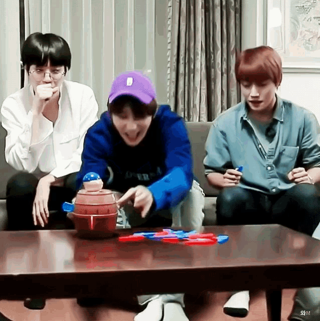three young men are sitting on a couch playing a game on a table