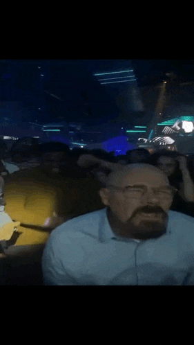 a man with glasses and a beard is sitting in a crowd of people