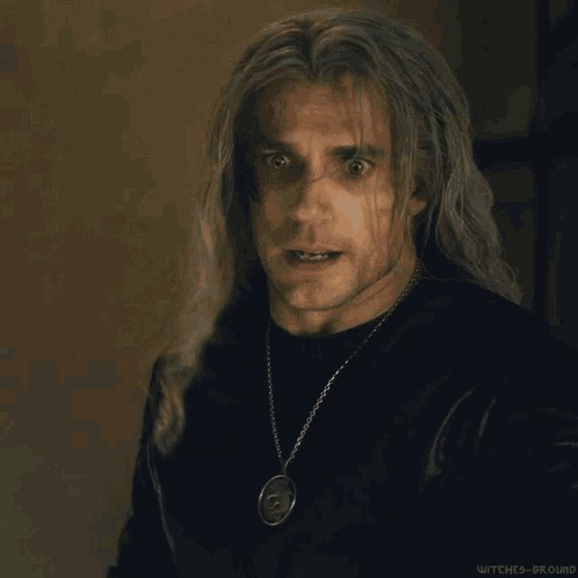 a man with long grey hair is wearing a black shirt and a necklace with a skull pendant .
