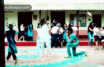 a man is kneeling down in front of a group of people dancing in a school hallway .