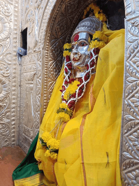a statue of a woman wearing a yellow cloth and garlands of flowers