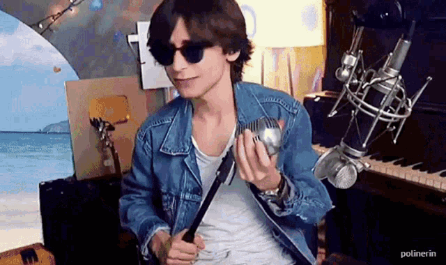 a man wearing sunglasses and a denim jacket is holding a microphone .