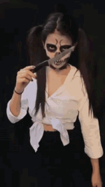 a woman with a skull face paint is holding a knife in her mouth .
