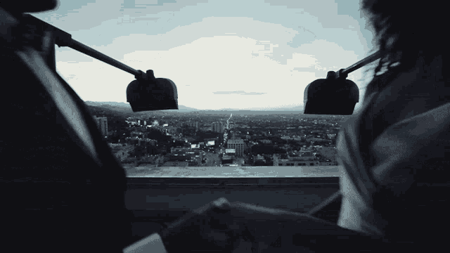 a person looking out a window at a city with mountains in the background