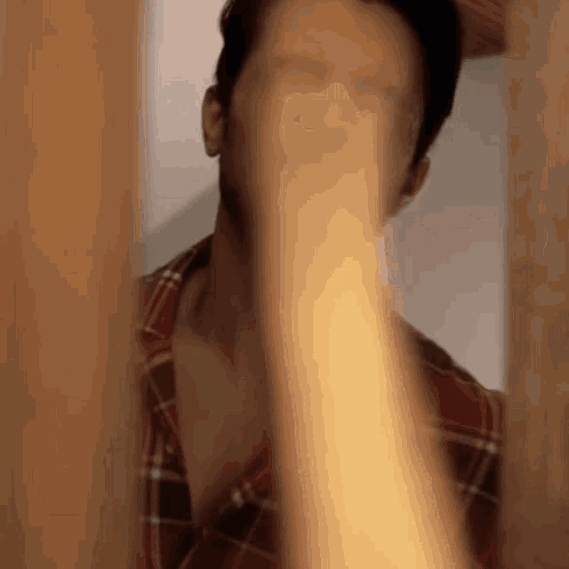 a man in a plaid shirt is covering his face with his hands