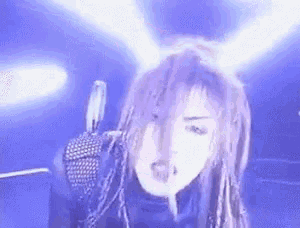 a woman with dreadlocks is singing into a microphone in front of a blue background .