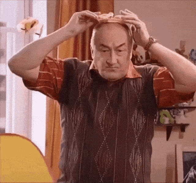 an older man wearing a sweater vest is putting a piece of food on his head .