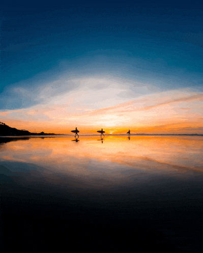 three surfers carrying their surfboards on the beach at sunset
