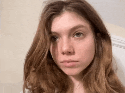 a young woman with long brown hair is looking at the camera with a sad look on her face .