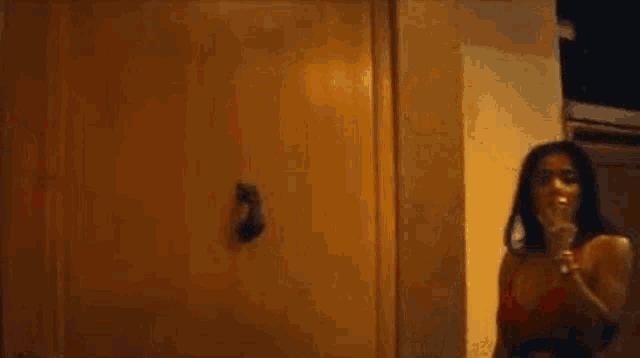 a woman in a red bra is standing in front of a door and smoking a cigarette .