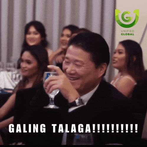 a man in a suit holds a glass in front of a group of women and says " galing talaga !!! "