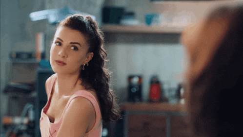 a woman in a pink top is looking at herself in a mirror