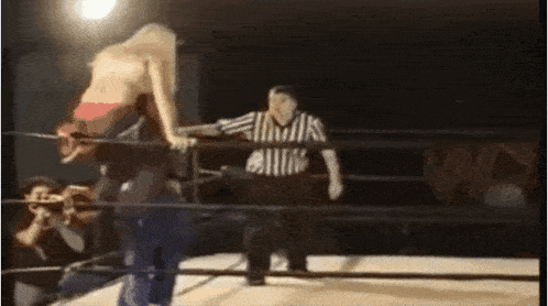 a woman in a wrestling ring with a referee standing behind her