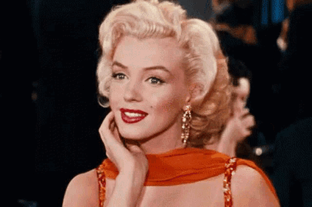 marilyn monroe is wearing a red dress and earrings and holding her hand to her face .