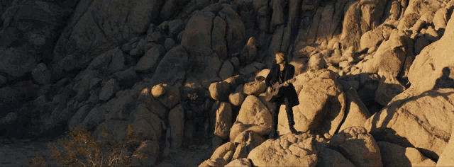 a man playing a guitar on top of a rocky cliff