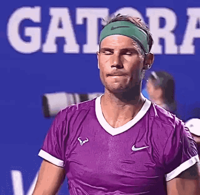 a tennis player wearing a purple shirt and a green headband is standing in front of a gatorade sign .
