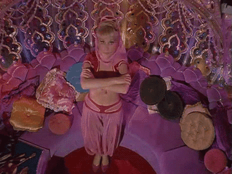 a woman in a pink costume is standing on a purple couch with her arms crossed .