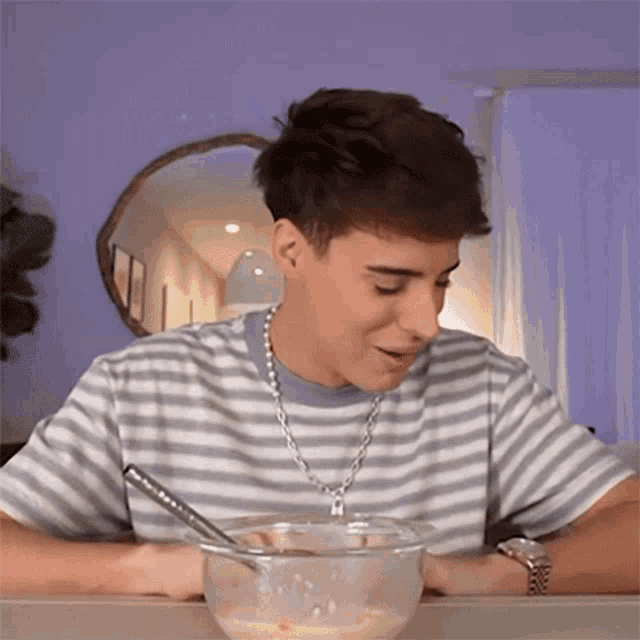 a young man is sitting at a table with a bowl of food and a spoon