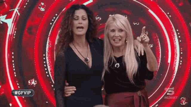 two women are standing next to each other in front of a red circle with the number 5 on it .