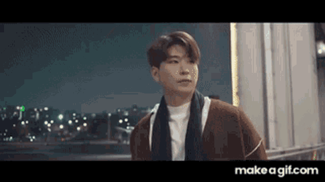 a man wearing a scarf and a sweater is standing in front of a building at night .