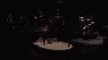 a group of people are dancing on a stage in a dark room while holding a tambourine .