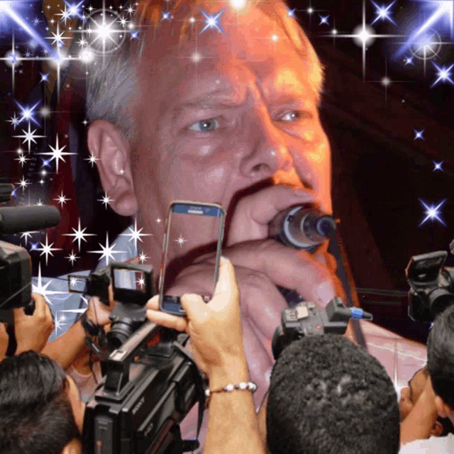 a man singing into a microphone is surrounded by cameras and people
