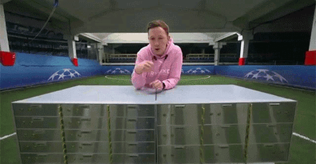 a man in a pink hoodie is standing in front of a table with a bunch of drawers on it .