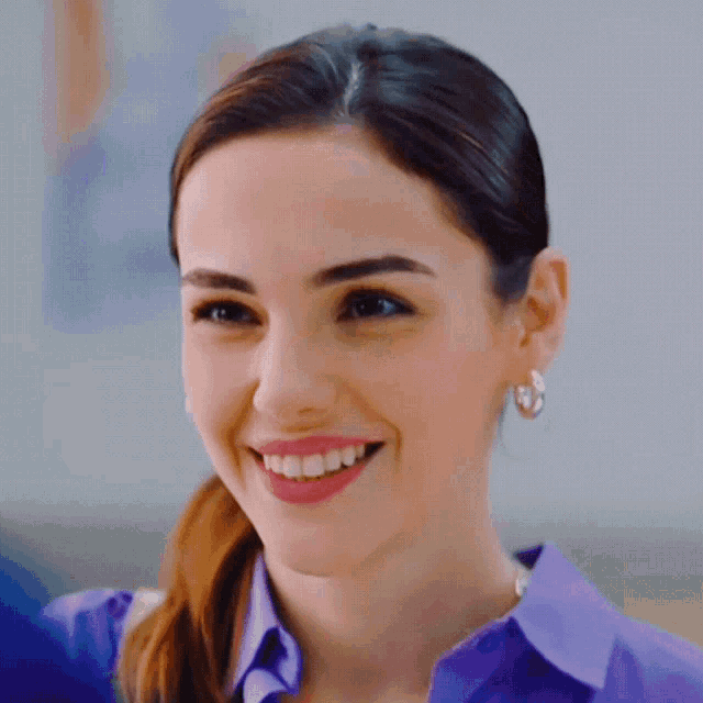 a woman wearing a purple shirt and hoop earrings is smiling