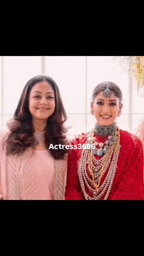 two women are posing for a picture together and smiling . one of the women is wearing a red dress .