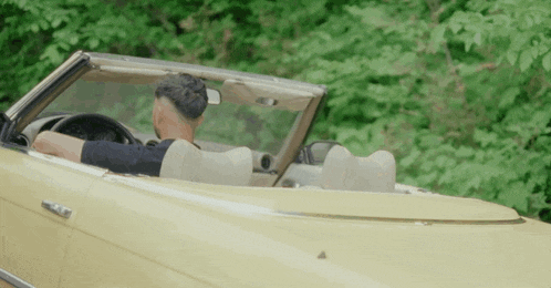 a man is driving a yellow convertible car with the top down .