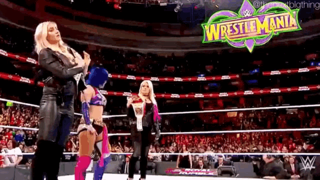 a group of women standing in a wrestling ring with a wrestlemania sign in the background