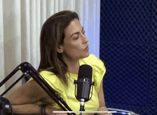 a woman in a yellow shirt is sitting in front of a black microphone