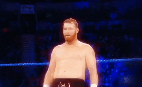 a shirtless wrestler is standing in a boxing ring and smiling .