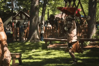 a man in a costume is standing in the grass in a park holding a sword .