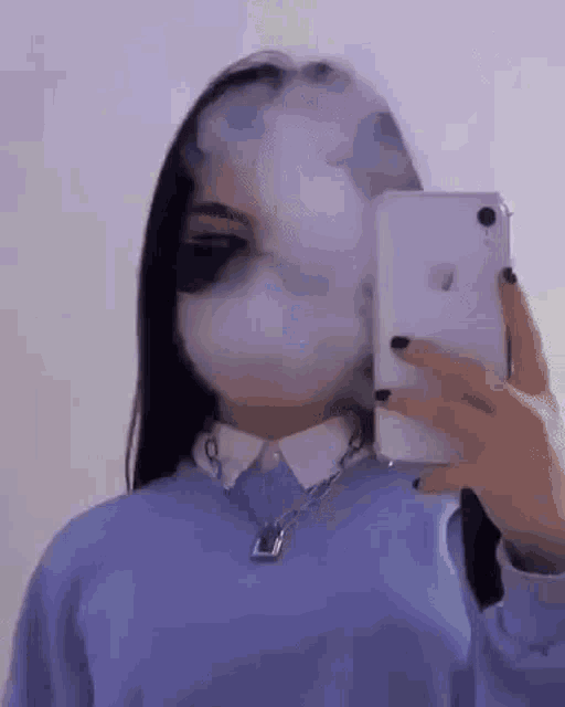 a girl is smoking a cigarette while taking a picture of herself in the mirror .