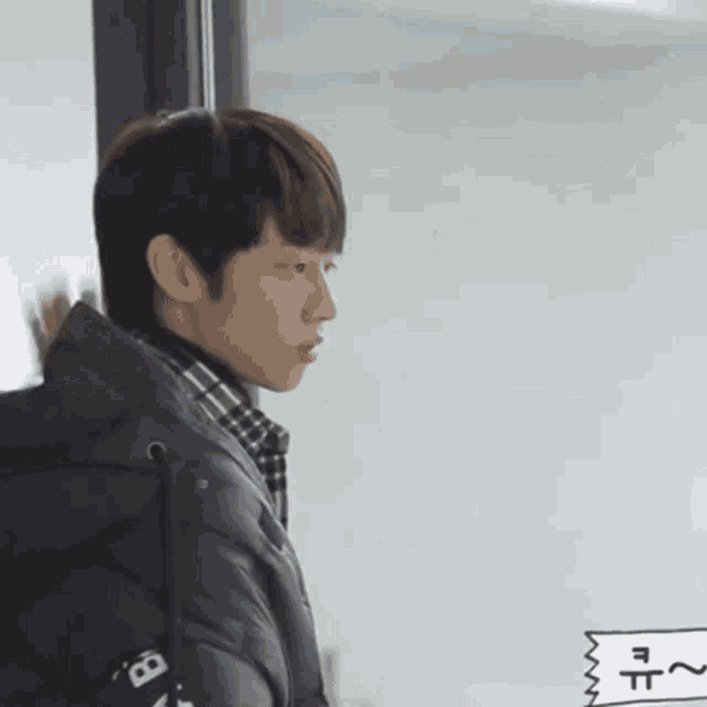 a young man wearing a black jacket and a plaid shirt is looking out of a window .
